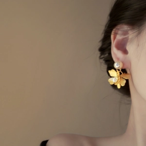 Elegant gold flower pearl earrings worn by a model in a sophisticated side profile view