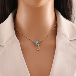 Close-up of golden necklace featuring a blue evil eye bead and a letter J pendant
