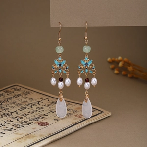 Macro detail of butterfly pearl tassel earrings with green drop pendant and gold frame