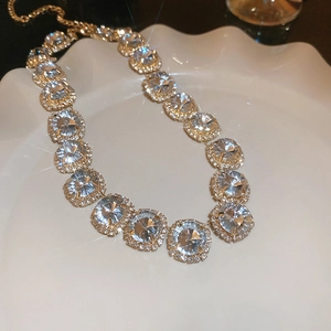 Close-up of golden necklace with clear crystals on a white wavy tray with soft lighting