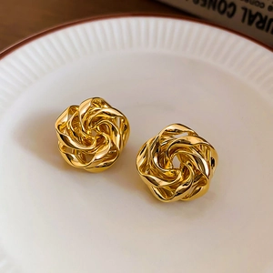 Dettaglio di orecchini a fiore in metallo dorato intrecciato in un piatto di ceramica