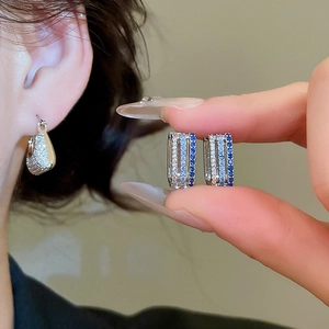 Detail of silver hoop earrings with blue and clear zircon stones in a triple row layout