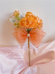 Detail of an orange carnation pen featuring organza bow with pearl on pink satin