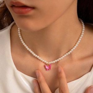 Detail of elegant white pearl necklace with a vibrant pink butterfly pendant on model