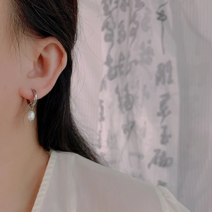 Close-up of minimalist silver stainless steel hoop earring with a hanging natural pearl