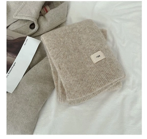 Close-up of soft beige knit wool scarf with minimalist egg brand label and woven texture