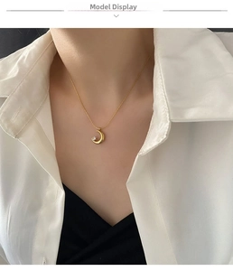 Detail of a minimalist gold moon pendant necklace with a crystal on a white shirt