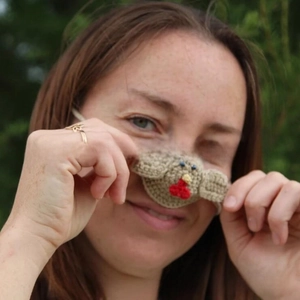 Macro detail of a handmade crochet rooster nose warmer with red comb and yellow beak accents