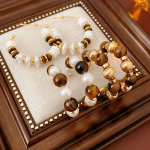 Detalle de pendientes en forma de C con piedras ojo de tigre, perlas y cuentas de oro