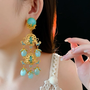 Close-up of vintage gold floral earrings with turquoise stones on a model's ear
