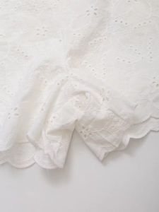 Detailed close-up of white cotton fabric with Broderie Anglaise and scalloped edges
