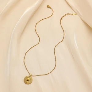 Macro detail of gold stainless steel necklace with Cancer zodiac coin pendant on silk