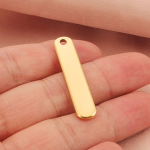 Macro shot of a polished gold stainless steel bar pendant held between fingers