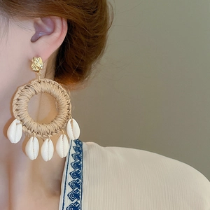Détail de boucles d'oreilles bohèmes en raphia tressé avec des coquillages sur un modèle