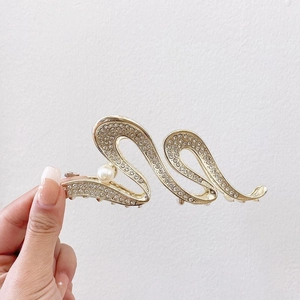 Detail of golden wave hair claw clip featuring sparkling rhinestones and a white pearl