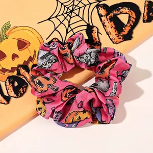Close-up of pink satin Halloween scrunchie with pumpkin and cat prints on orange cloth