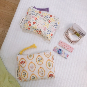 Detail of floral cotton pouches with zipper tassels and brand label on fabric background
