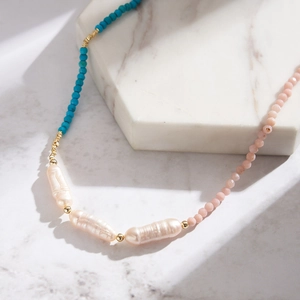 Detailed view of handmade beaded necklace with baroque pearls and colorful stones on marble