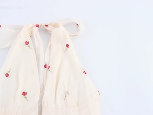 Detail showing red rose floral embroidery on a cream halter neck backless dress