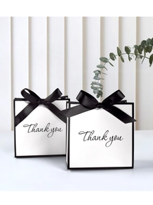 Detail of white gift bag with black silk bow and Thank You cursive text in a luxury setting