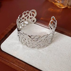 Close-up of silver hollowed-out cuff bracelet with intricate floral vine patterns on linen