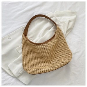 Detail of beige woven straw shoulder bag with brown PU leather strap on white fabric