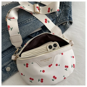 Detail view of white faux leather crossbody bag with red cherry print and golden hardware