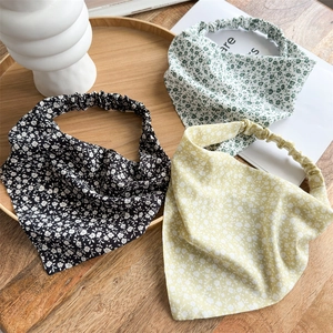 Close-up of floral chiffon hair scarves in black, green, and yellow on a wooden tray