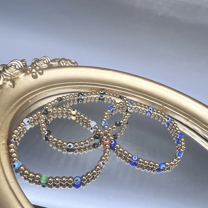 Macro detail of 18K gold plated evil eye beaded bracelets on a vintage golden mirror