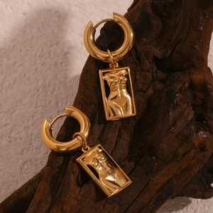 Detailed relief of female body art pendant on a gold rectangular earring set on wood