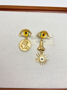 Detail of artistic gold earrings set featuring eye, nose, and coin charms on white canvas