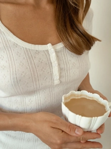 Detail of white hollow knit top with diamond patterns and buttons in a lifestyle setting