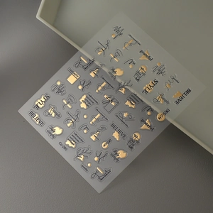 Macro detail of gold foil nail stickers with elegant lettering and minimalist line art