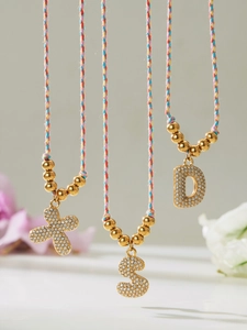 Détail de colliers tressés colorés avec pendentifs lettres en or 18K et zircons