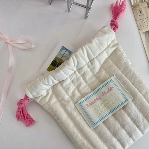 Close-up of a quilted cream storage bag with pink drawstrings and embroidered patch