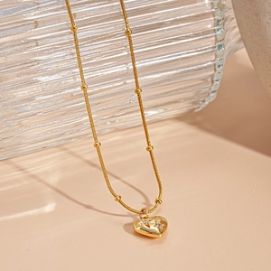 Makroaufnahme einer goldfarbenen Perlenkette mit Herzanhänger und Zirkonia-Gravur