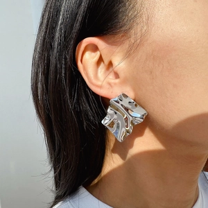 Irregular wrinkled geometric silver metal earrings on a model with mirror finish