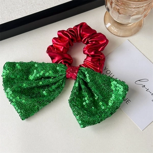 Close-up of a festive red hair scrunchie with a green sequin bow and gold bell detail