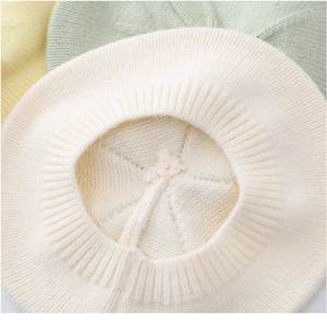 Detail shot of the cream-colored knitted baby beret showing intricate texture and soft fabric