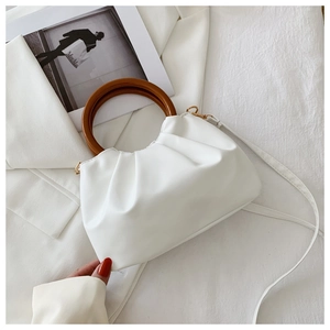 Detail of white pleated cloud bag with round wooden handle and gold metal hardware