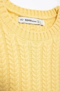 Dettaglio ravvicinato di maglione giallo a maglia con girocollo e trama a trecce