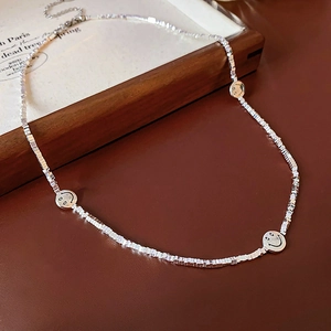 Detail of silver smiley face necklace with square metal beads on brown leather surface