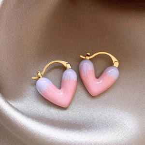 Detailed macro of gold heart earrings with pink enamel finish on champagne silk