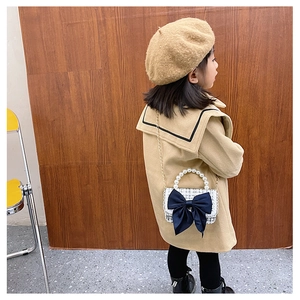 Detail of girl wearing plaid crossbody bag with pearl handle and bow decoration
