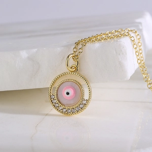 Golden necklace with a pink evil eye pendant featuring zircon accents on marble surface