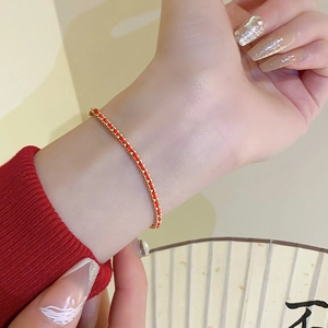 Close-up of hand-woven red string bracelet with gold beads worn on a wrist