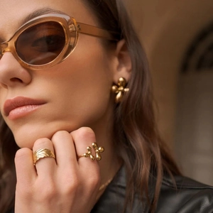 Detailed view of sculptural golden earrings and leaf-shaped rings on model in natural light