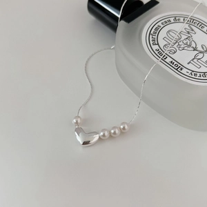 Macro detail of a minimalist 925 sterling silver heart necklace with four white pearls