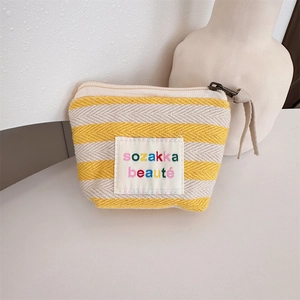 Detail of yellow striped canvas pouch with embroidered patch and metal zipper closure