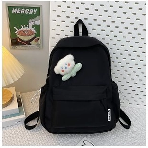 Detail of black nylon school backpack featuring front zipper pocket and plush bear pendant
